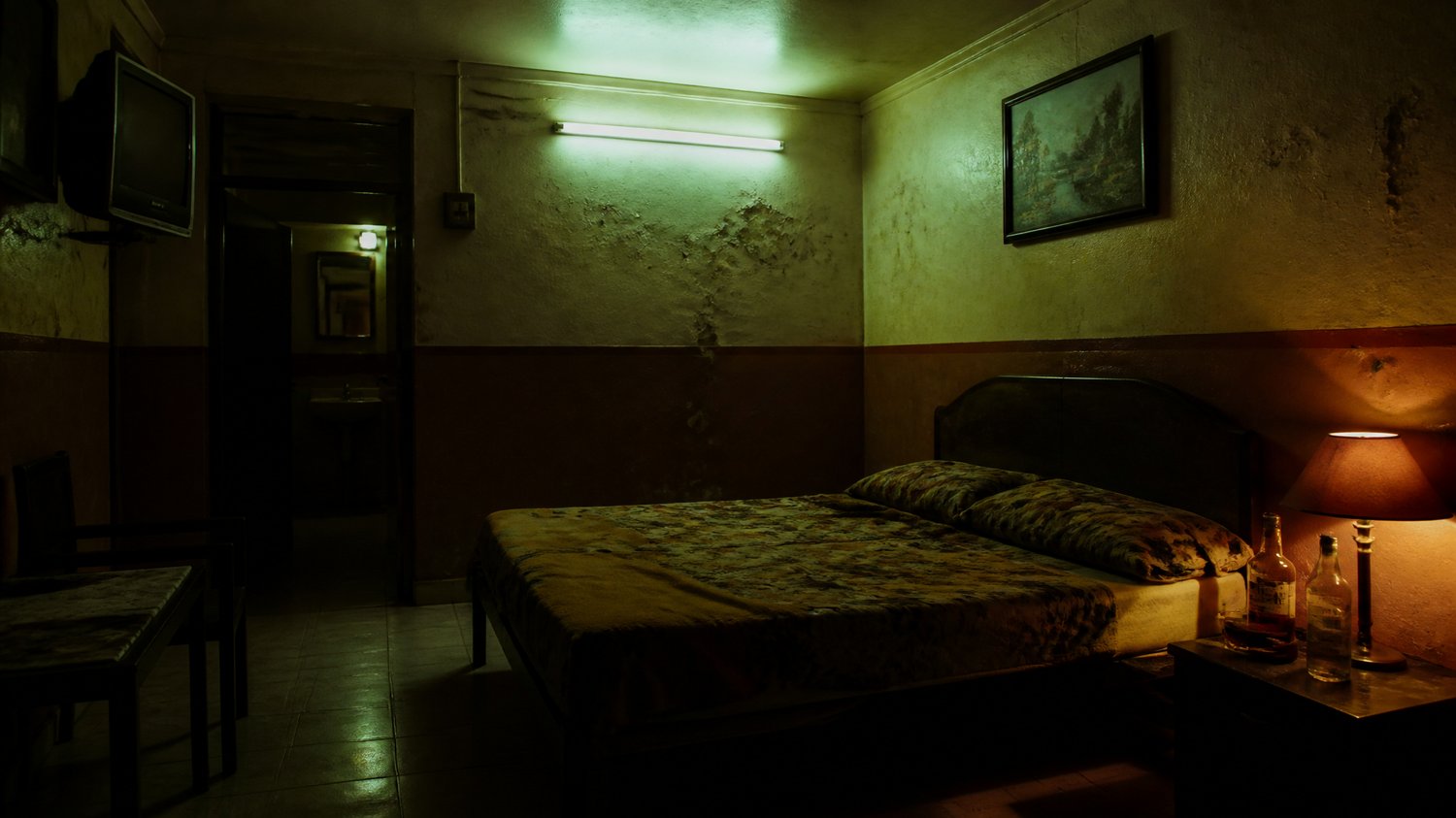 Adventure Motel — A cheap hourly motel: peeling paint, a buzzing tube-light, a sagging bed, a whisky bottle, no CCTV — chosen for exactly that. Where the ritual unfolds.